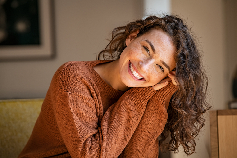Happy young woman sitting on sofa at home and looking at camera - Cosmetic Dentistry Happy young woman sitting on sofa at home and looking at camera - Cosmetic Dentistry