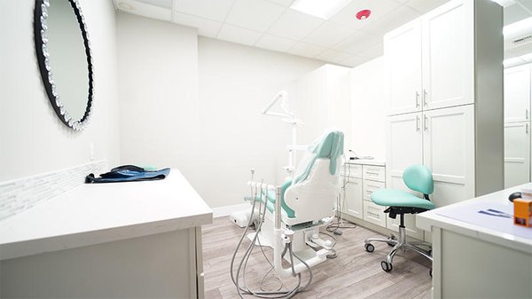 A clean, modern dental treatment room with a mint-green dental chair, cabinetry, and a round wall mirror - Dentist Federal Way WA A clean, modern dental treatment room with a mint-green dental chair, cabinetry, and a round wall mirror - Dentist Federal Way WA