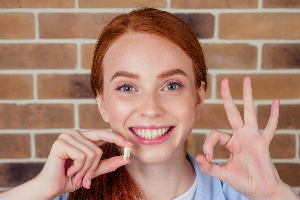 female with snow white smile holding white wisdom tooth - tooth extractions female with snow white smile holding white wisdom tooth - tooth extractions